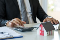 Real estate agent with a calculator and model of the house on the table