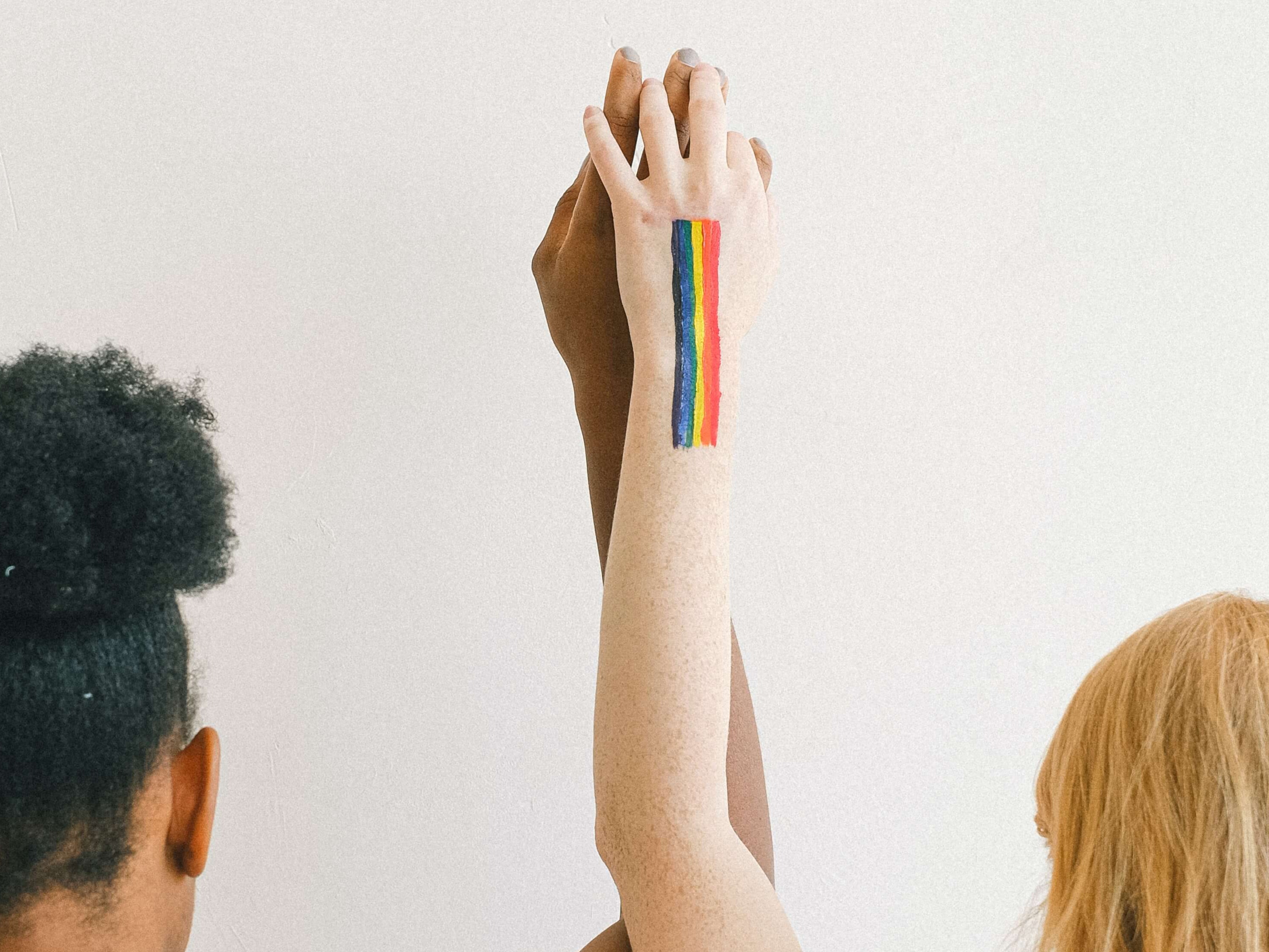 two people holding hands with LGBTQ flag painted on one arm